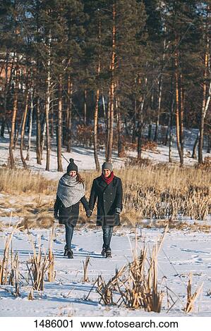 Young couple holding hands while walking on snow covered field View Large Photo Image Stock Image - Young couple holding hands while walking on snow covered field. Fotosearch