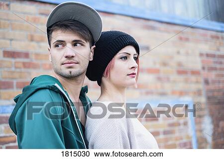 Stock Image - Young couple standing against brick wall. Fotosearch