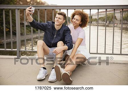 Young couple taking selfie with camera phone on urban bridge View Large Photo Image Stock Photography - Young couple taking selfie with camera phone on urban bridge. Fotosearch