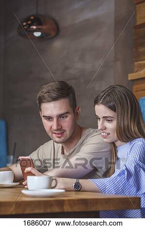 Young couple using mobile phone while sitting at restaurant View Large Photo Image Stock Photo - Young couple using mobile phone while sitting at restaurant. Fotosearch
