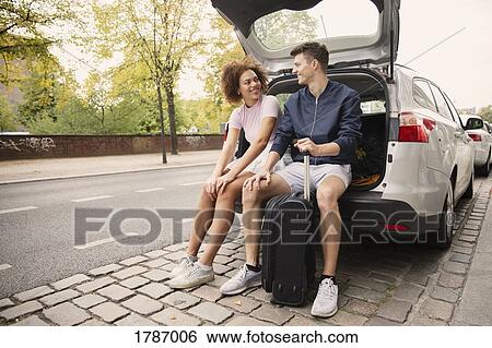 Stock Photograph - Young couple with suitcase sitting in car hatchback. Fotosearch
