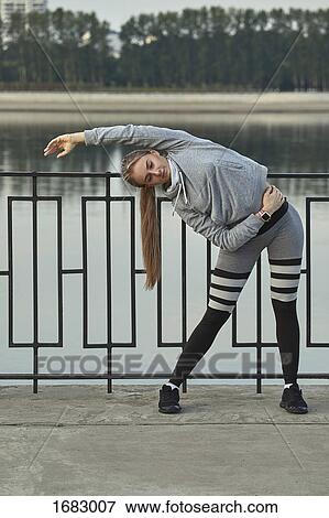 Young female athlete exercising on footpath against lake View Large Photo Image Stock Photo - Young female athlete exercising on footpath against lake. Fotosearch