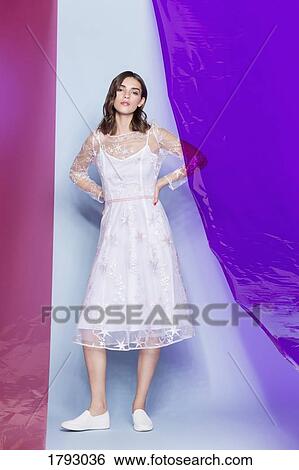 Stock Photograph - Young female fashion model wearing white dress and posing with colored panels. Fotosearch