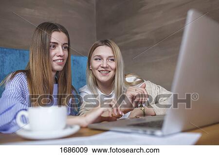 Young female friends using laptop while sitting in restaurant View Large Photo Image Stock Photo - Young female friends using laptop while sitting in restaurant. Fotosearch