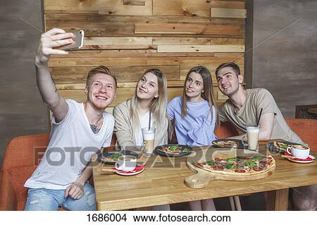 Young friends taking selfie while sitting at restaurant View Large Photo Image Picture - Young friends taking selfie while sitting at restaurant. Fotosearch