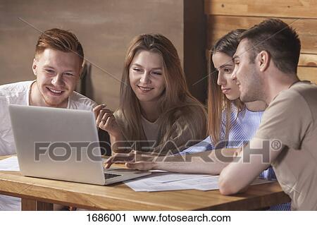 Stock Image - Young friends using laptop while sitting at restaurant. Fotosearch