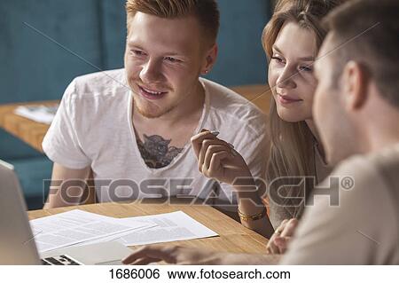 Stock Photograph - Young friends using laptop while sitting at table in restaurant. Fotosearch