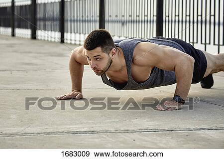 Stock Photo - Young male athlete practicing push-ups on footpath. Fotosearch