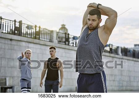 Young male athlete stretching with friends in background against bridge View Large Photo Image Stock Photography - Young male athlete stretching with friends in background against bridge. Fotosearch