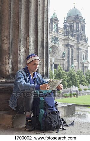 Stock Image - Young male tourist sitting with map at Altes Museum against Berlin Cathedral, Germany. Fotosearch