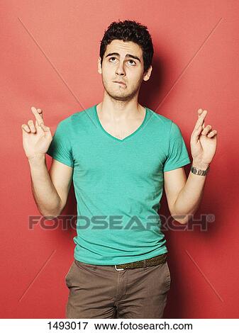Young man crossing fingers while looking up against red background View Large Photo Image Stock Photo - Young man crossing fingers while looking up against red background. Fotosearch