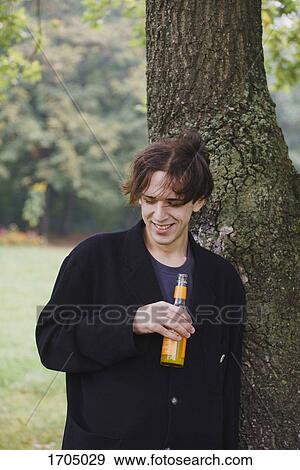Young man drinking juice while standing by tree View Large Photo Image Stock Photo - Young man drinking juice while standing by tree. Fotosearch