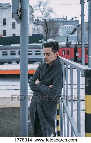 Young man in coat standing at winter railroad station View Large Photo Image Picture - Young man in coat standing at winter railroad station. Fotosearch