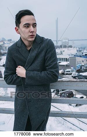 Young man in long coat on urban winter bridge View Large Photo Image Stock Photo - Young man in long coat on urban winter bridge. Fotosearch
