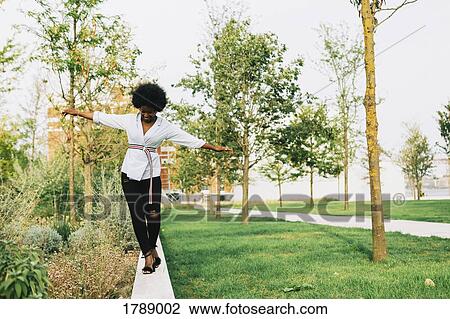Young woman balancing on ledge in park View Large Photo Image Stock Image - Young woman balancing on ledge in park. Fotosearch