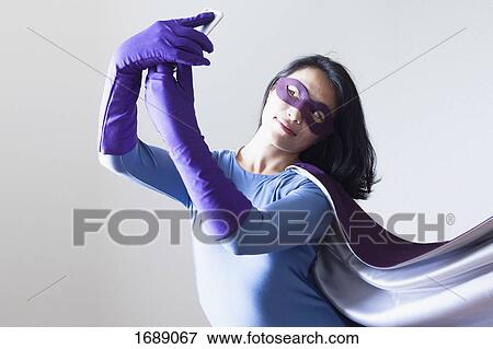 Young woman dressed as superhero taking selfie against white background View Large Photo Image Stock Photo - Young woman dressed as superhero taking selfie against white background. Fotosearch
