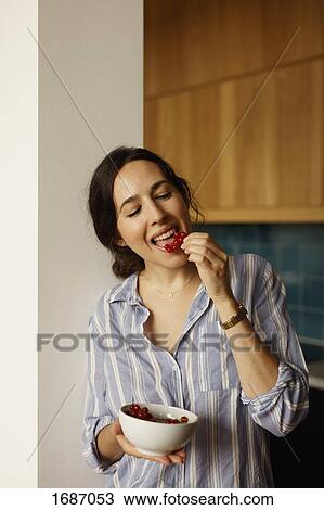 Stock Image - Young woman eating red currants at home. Fotosearch