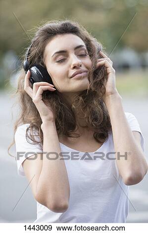 Stock Photo - Young woman enjoying listening music outdoors. Fotosearch