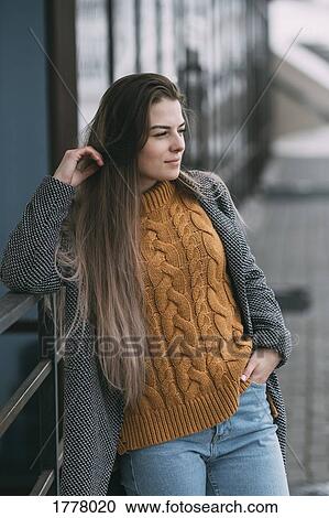 Stock Image - Young woman leaning against railing, looking away. Fotosearch