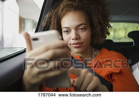 Picture - Young woman listening to music with headphones and mp3 player in car. Fotosearch