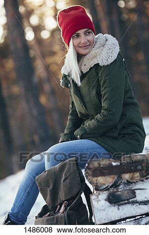Young woman looking away while sitting on log during winter View Large Photo Image Stock Photo - Young woman looking away while sitting on log during winter. Fotosearch