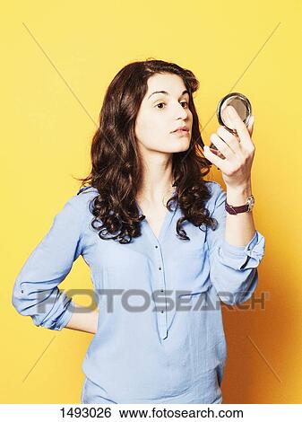 Young woman looking in powder compact mirror against yellow background View Large Photo Image Stock Photograph - Young woman looking in powder compact mirror against yellow background. Fotosearch