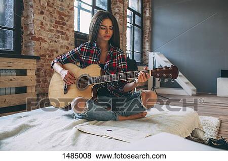 Young woman playing guitar while sitting on bed at home View Large Photo Image Stock Photo - Young woman playing guitar while sitting on bed at home. Fotosearch