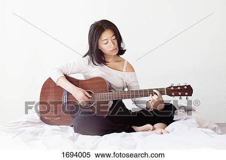 Young woman playing guitar while sitting on bed at home View Large Photo Image Stock Photography - Young woman playing guitar while sitting on bed at home. Fotosearch