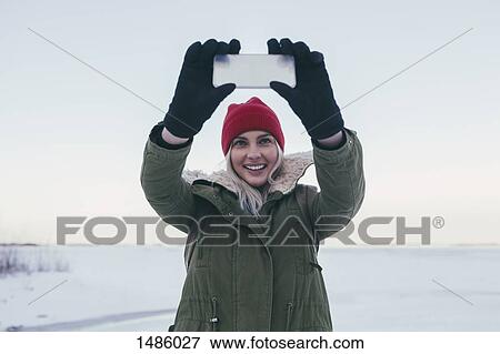 Young woman taking selfie on smart phone during winter View Large Photo Image Stock Photo - Young woman taking selfie on smart phone during winter. Fotosearch