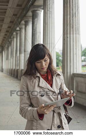 Stock Photograph - Young woman using digital tablet while walking in corridor, Berlin, Germany. Fotosearch