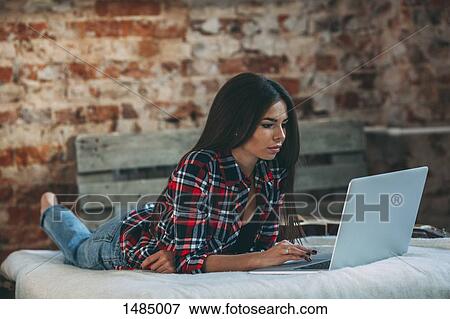 Young woman using laptop while lying on bed at home View Large Photo Image Stock Photo - Young woman using laptop while lying on bed at home. Fotosearch