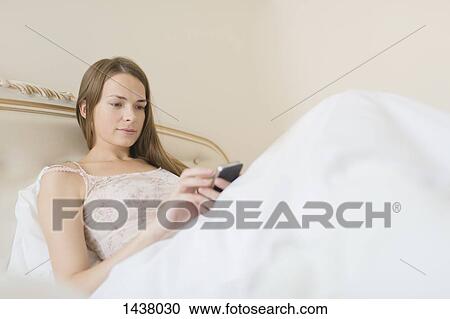 Young woman using smart phone in bed at home View Large Photo Image Stock Image - Young woman using smart phone in bed at home. Fotosearch
