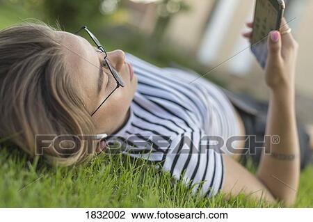 Young woman using smart phone in grass View Large Photo Image Stock Image - Young woman using smart phone in grass. Fotosearch