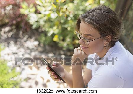 Young woman using smart phone in park View Large Photo Image Stock Photography - Young woman using smart phone in park. Fotosearch