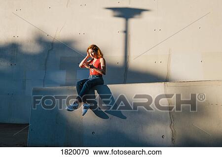 Stock Image - Young woman using smart phone on urban wall. Fotosearch