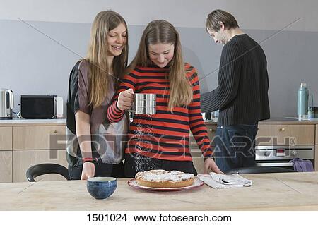 Young woman watching sister sprinkling tart with icing sugar in kitchen View Large Photo Image Picture - Young woman watching sister sprinkling tart with icing sugar in kitchen. Fotosearch