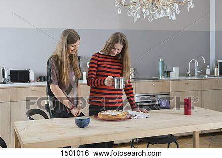 Young woman watching sister sprinkling tart with icing sugar in kitchen View Large Photo Image Stock Photograph - Young woman watching sister sprinkling tart with icing sugar in kitchen. Fotosearch
