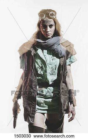 Stock Image - Young woman wearing jacket holding gun against white background. Fotosearch
