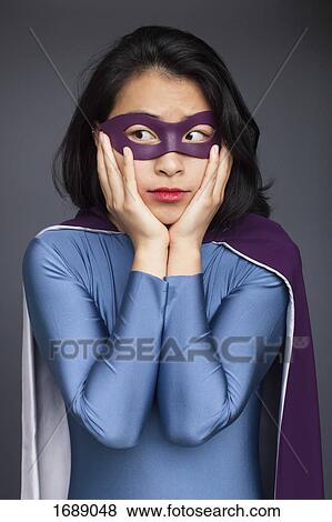Young woman wearing superhero costume standing with head in hands against gray background View Large Photo Image Stock Photo - Young woman wearing superhero costume standing with head in hands against gray background. Fotosearch