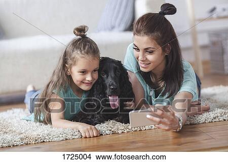 Young woman with daughter and dog taking selfie using smart phone at home View Large Photo Image Picture - Young woman with daughter and dog taking selfie using smart phone at home. Fotosearch