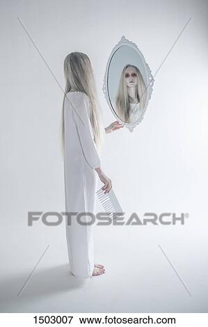 Young woman with spooky red eyes looking in mirror against white background View Large Photo Image Stock Photo - Young woman with spooky red eyes looking in mirror against white background. Fotosearch