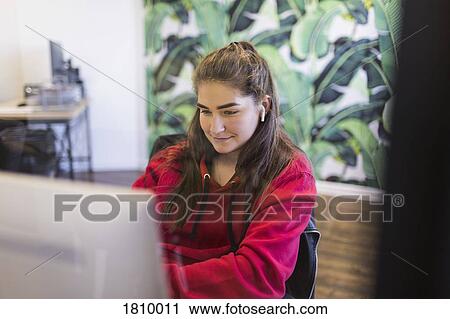 Stock Image - Young woman with wireless earbuds using computer in internet cafe. Fotosearch