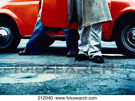 couple standing in front of ornage car View Large Photo Image Stock Image - couple standing in front of ornage car. Fotosearch