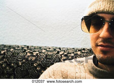 Stock Photo - man sitting on couch wearing sunglasses and hat. Fotosearch