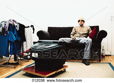 man sitting on couch wearing sunglasses and hat watching tv View Large Photo Image Stock Photo - man sitting on couch wearing sunglasses and hat watching tv. Fotosearch