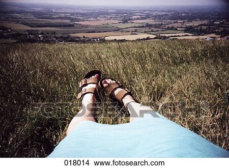 Picture - a woman's legs and feet outstretched in grass overlooking fields. Fotosearch
