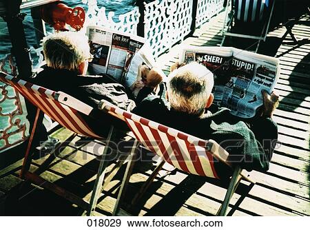 two men sitting in beach chairs reading newspapers View Large Photo Image Stock Photo - two men sitting in beach chairs reading newspapers. Fotosearch