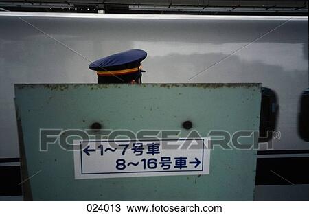 Stock Image - A train conductor between a sign with Japanese writing and a train. Fotosearch