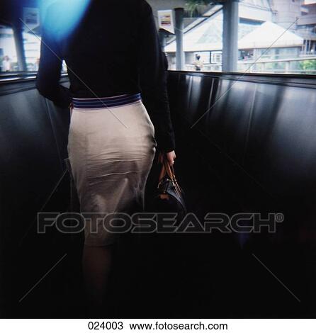 Stock Image - View of a woman from behind, walking down a corridor. Fotosearch