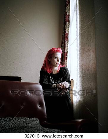 Stock Image - A woman with pink hair sitting in a room looking out a window. Fotosearch